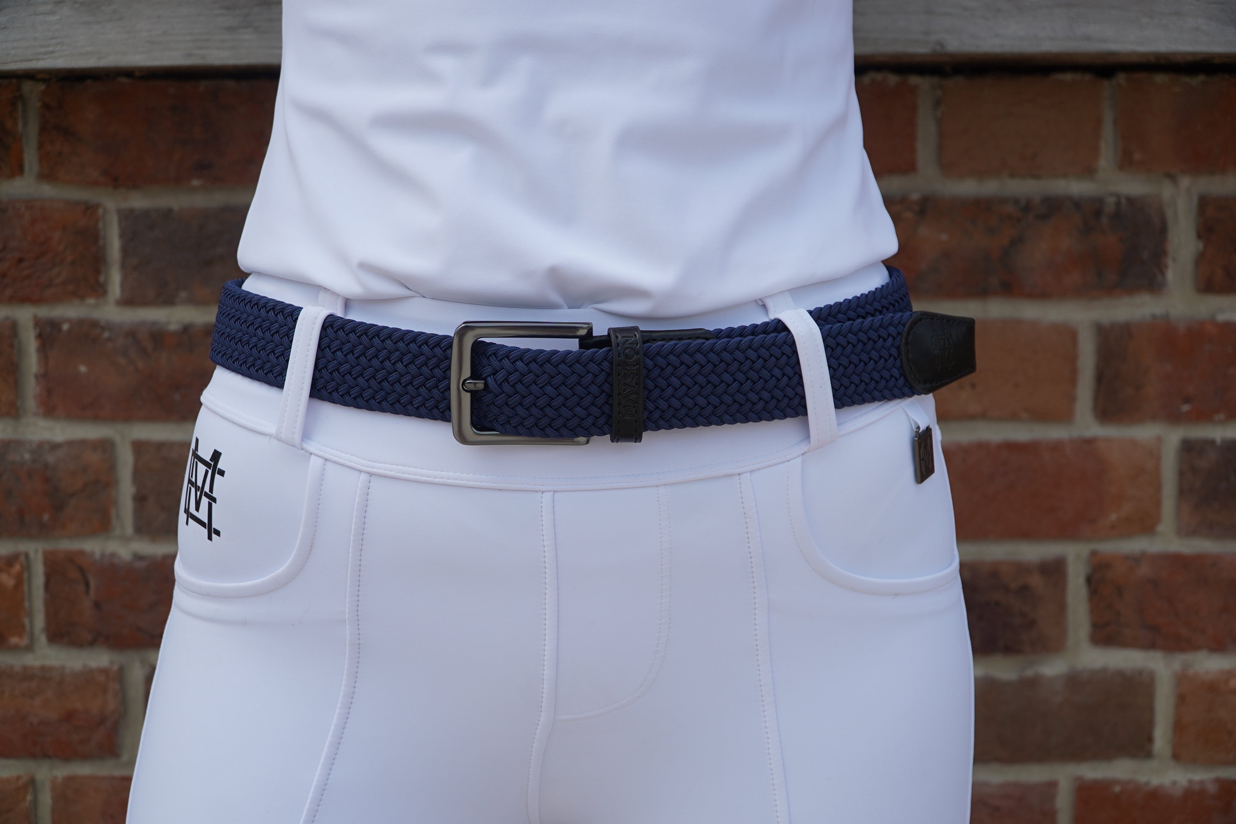 White pants with a navy belt and black buckle against a brick wall. Elastic stretch quality belt for casual or riding wear