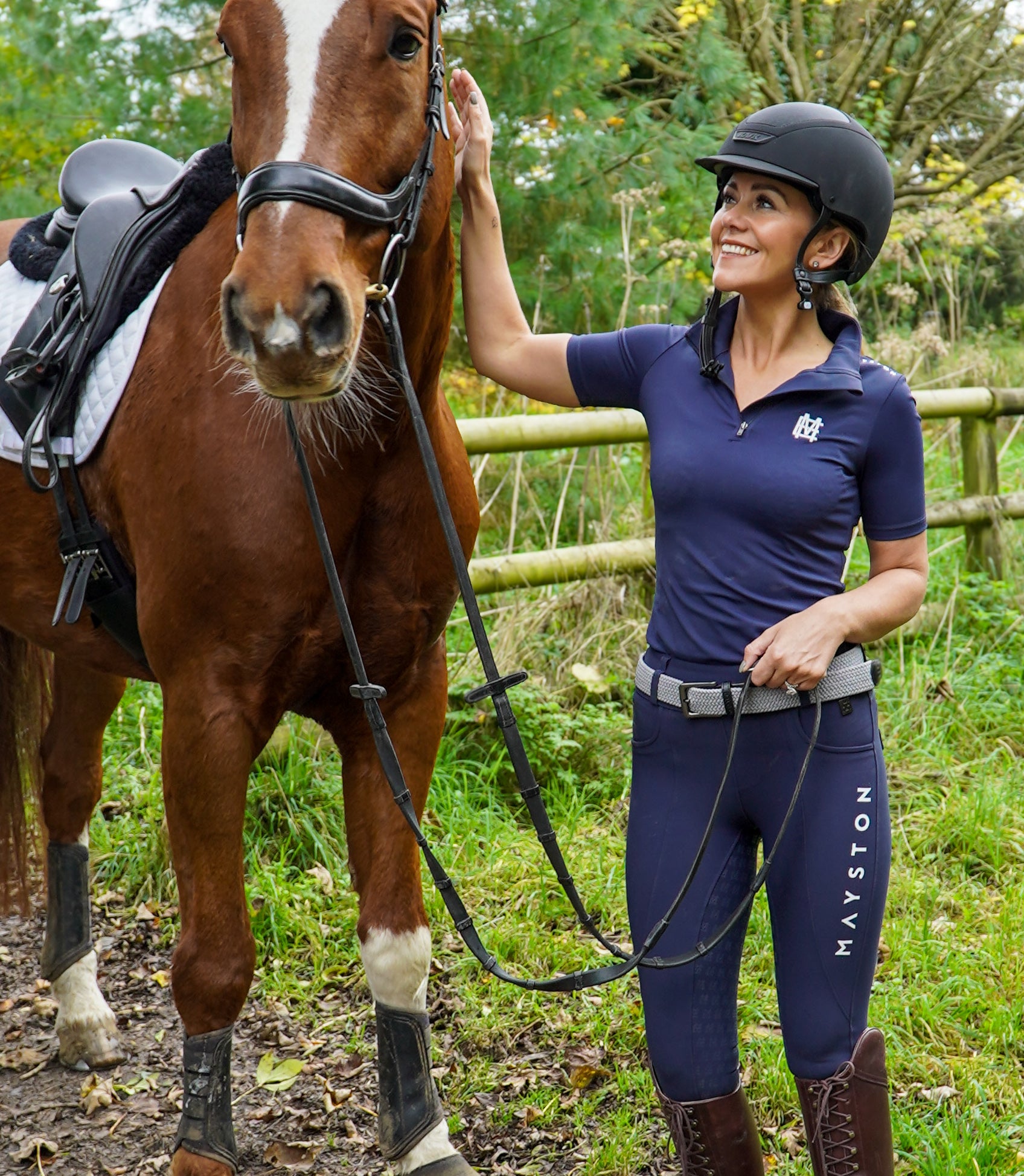 Sleek silhouette baselayer top subtle Mayston branding, maximum coverage without compromising style, next-level performance with a bold, minimalist look. Moisture-wicking, breathable fabric with four-way stretch, it keeps you cool and comfortable. Training, Everyday or competition wear. Short Sleeve 1/4 zip with collar. navy with white branding. woman stood smiling with horse