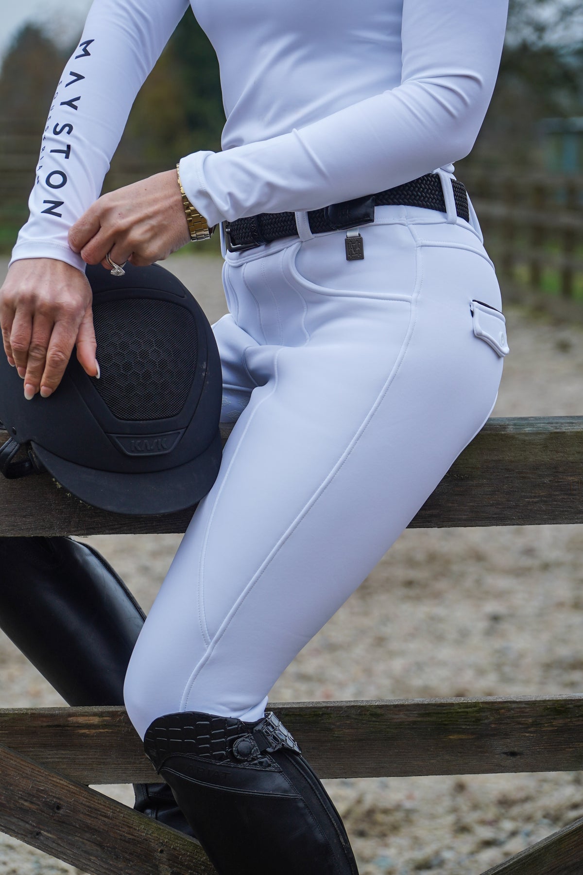 Person wearing white riding pants and black boots, sitting on a wooden fence. stretch white breeches, winter fleece lined. full seat silicone