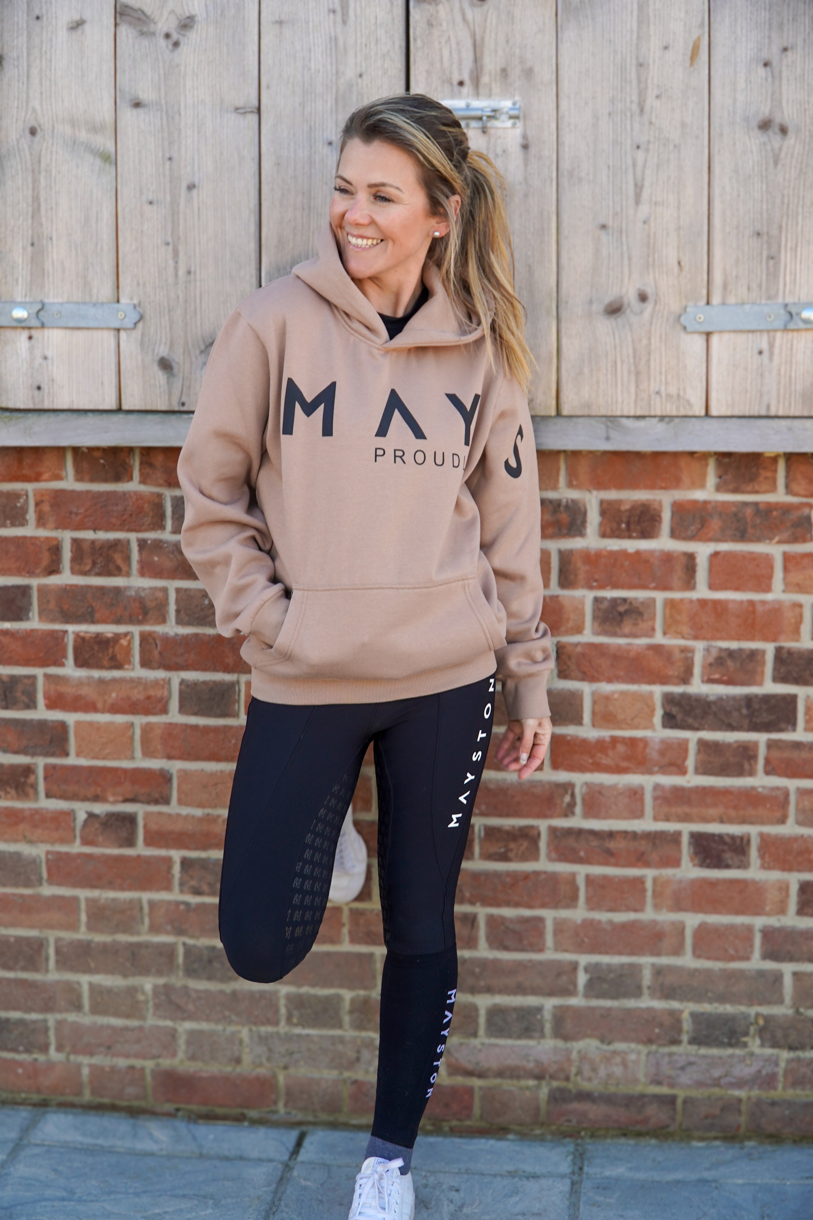 A person wearing a beige brown hoodie with 'MAY' printed on the front in large letters, paired with black leggings and white shoes, standing in front of a wooden background.
High quality luxurious 100% cotton. wrap around bold logo. soft, cozy and warm. Hoodie, jumper sweatshirt. everyday wear. casual and smart