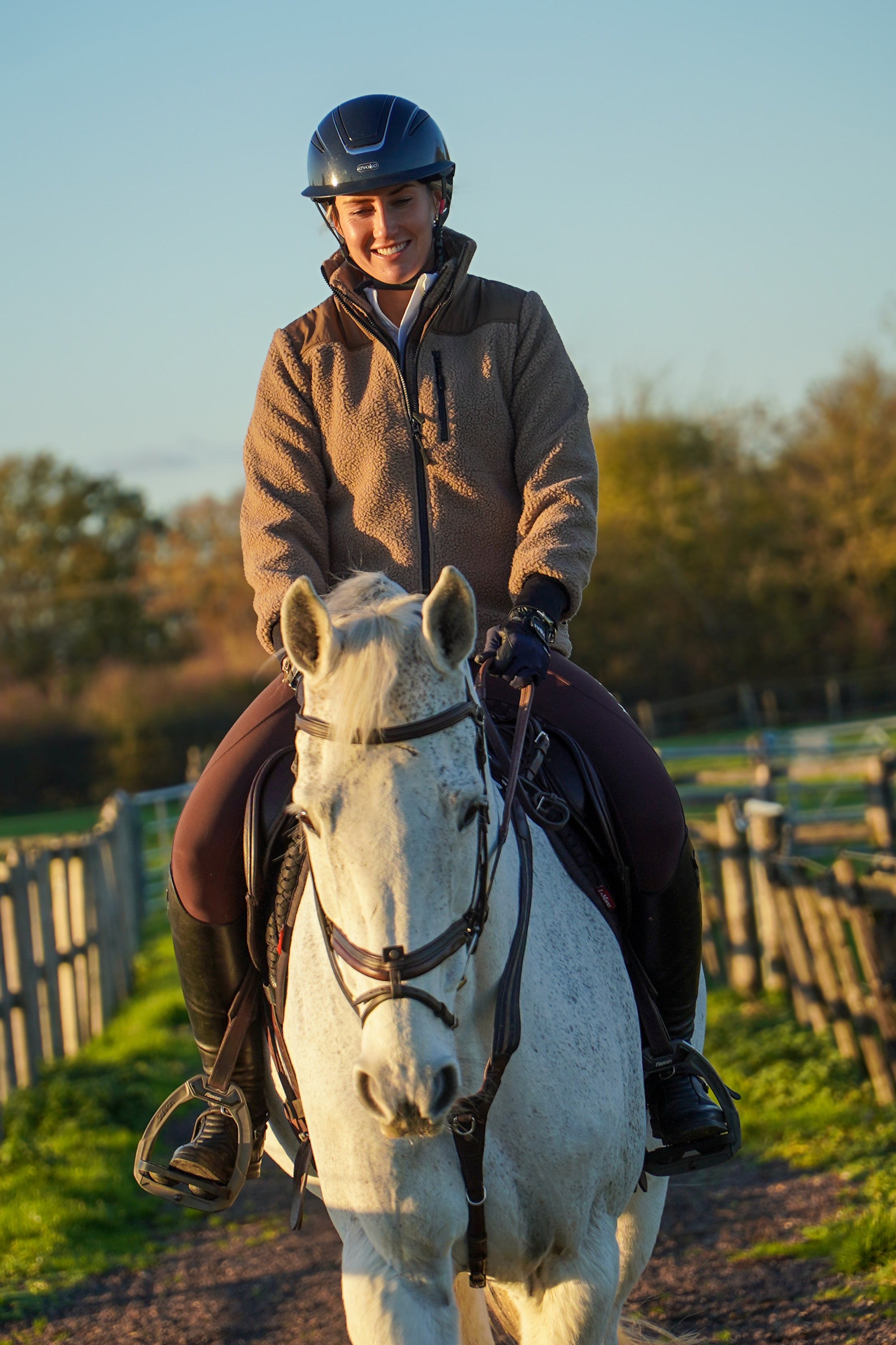 Person riding a white horse in an outdoor setting with trees and a fence in the background. warm teddy fleece jacket