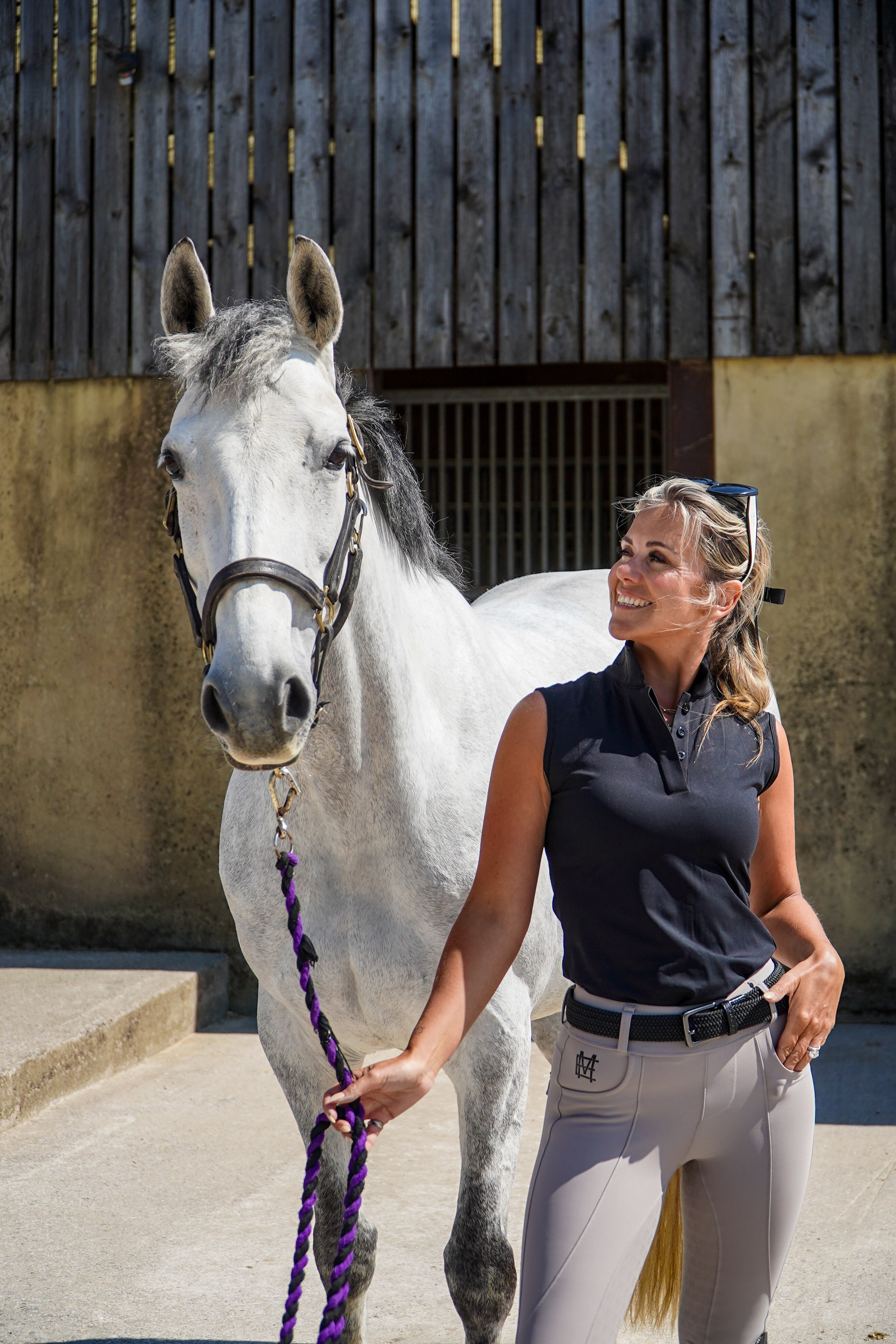 Woman in equestrian attire standing next to a white horse in an outdoor setting. Ultra-soft technical sport fabric. Breathable and lightweight for warmer weather. Flattering athletic fit
Signature black branded Mayston collar. Subtle gloss shoulder logo detail. Sleeveless design for unrestricted movement. blackout colour match branding