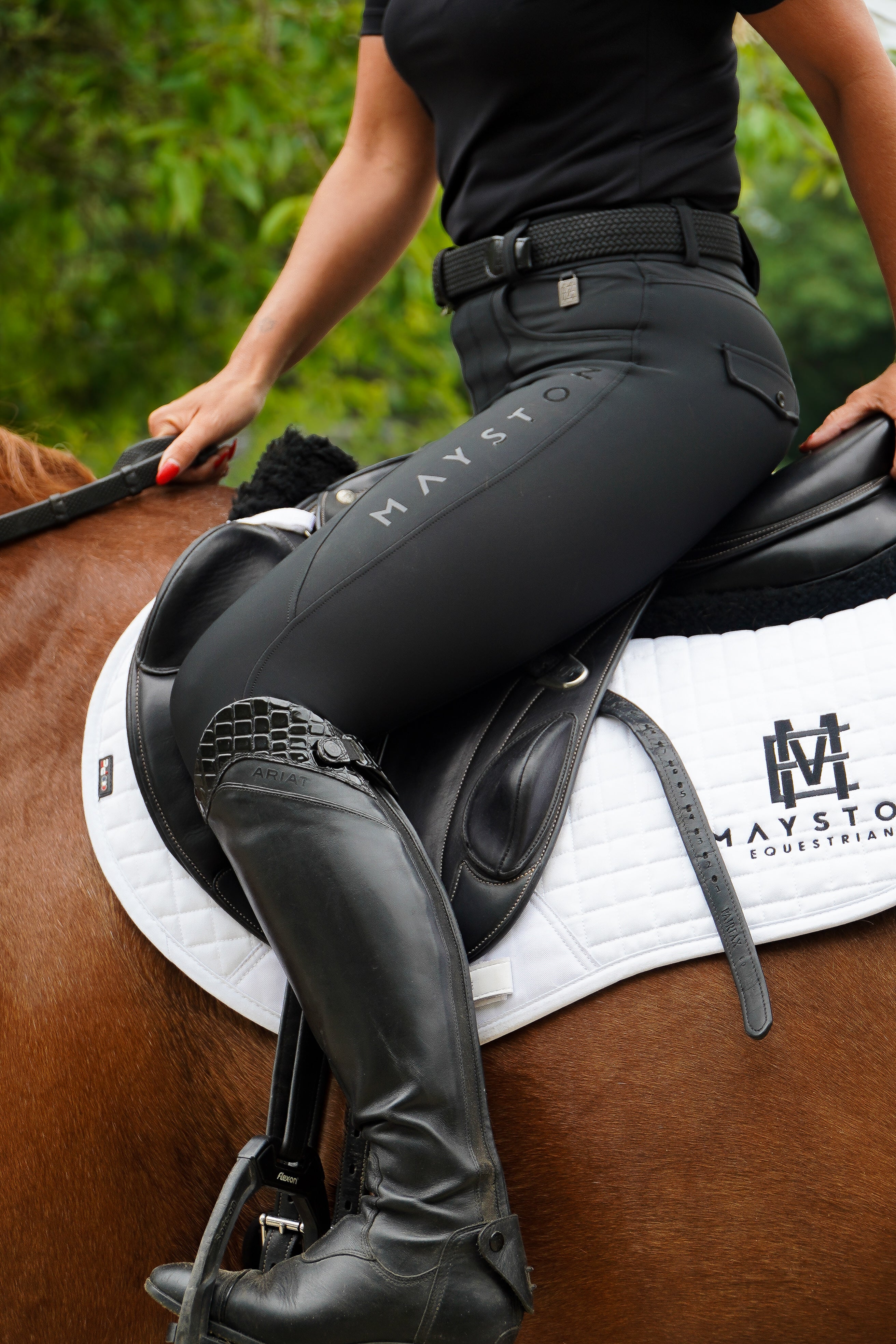 Person riding a horse wearing black Maystone riding pants and boots. Premium Black breeches with a Full Silicone seat. Stretch high waisted Jodhpurs. Deep pockets, supportive, comfortable and compression quality fabric. Elegant detailing with subtle branding.  