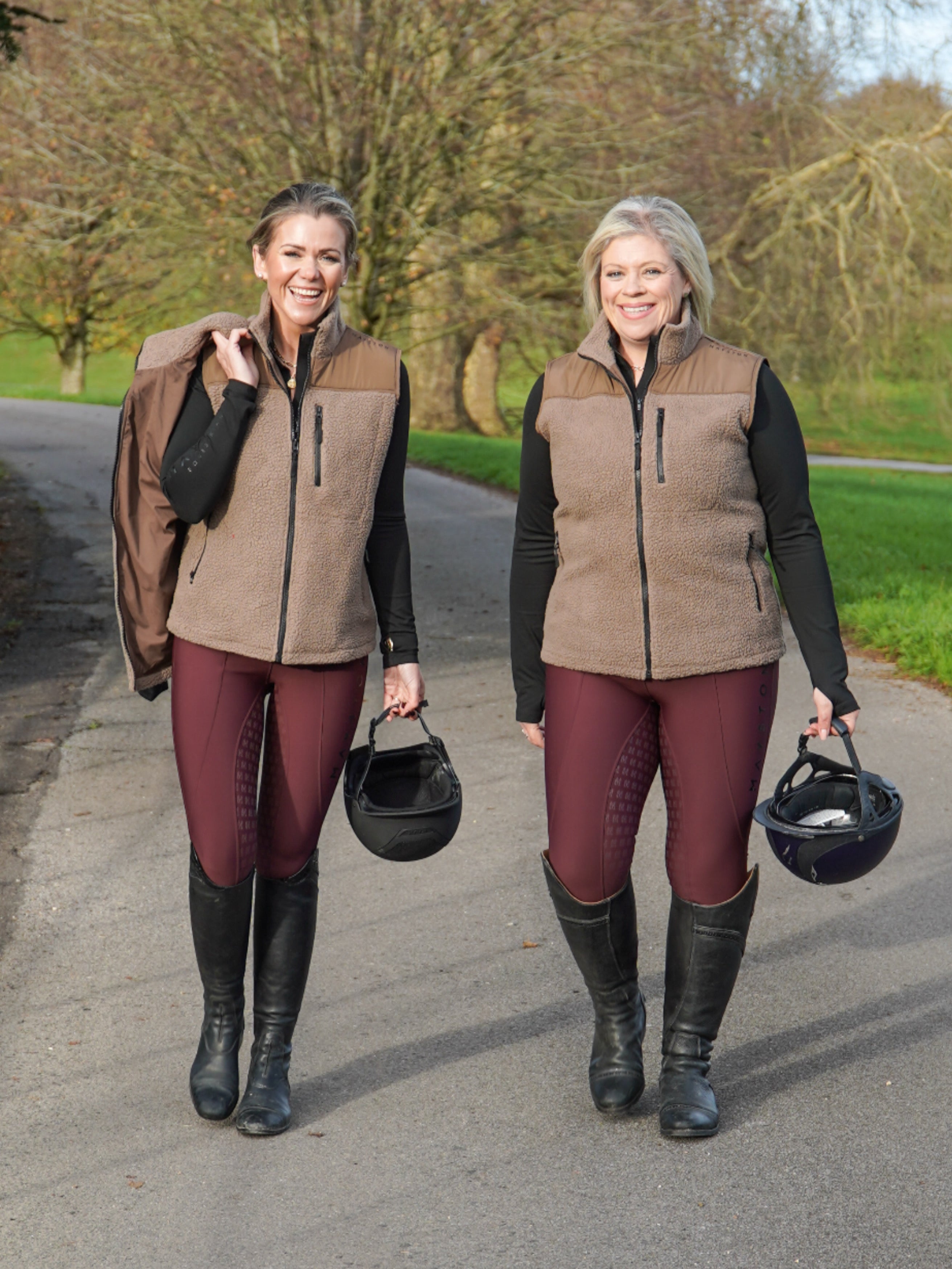 Two women in equestrian attire walking outdoors on a path. Luxury teddy Fleece Gilet Waistcoat. Quality embroidery. multiple pockets. Subtle branding, elegant classic design. Stretch lining