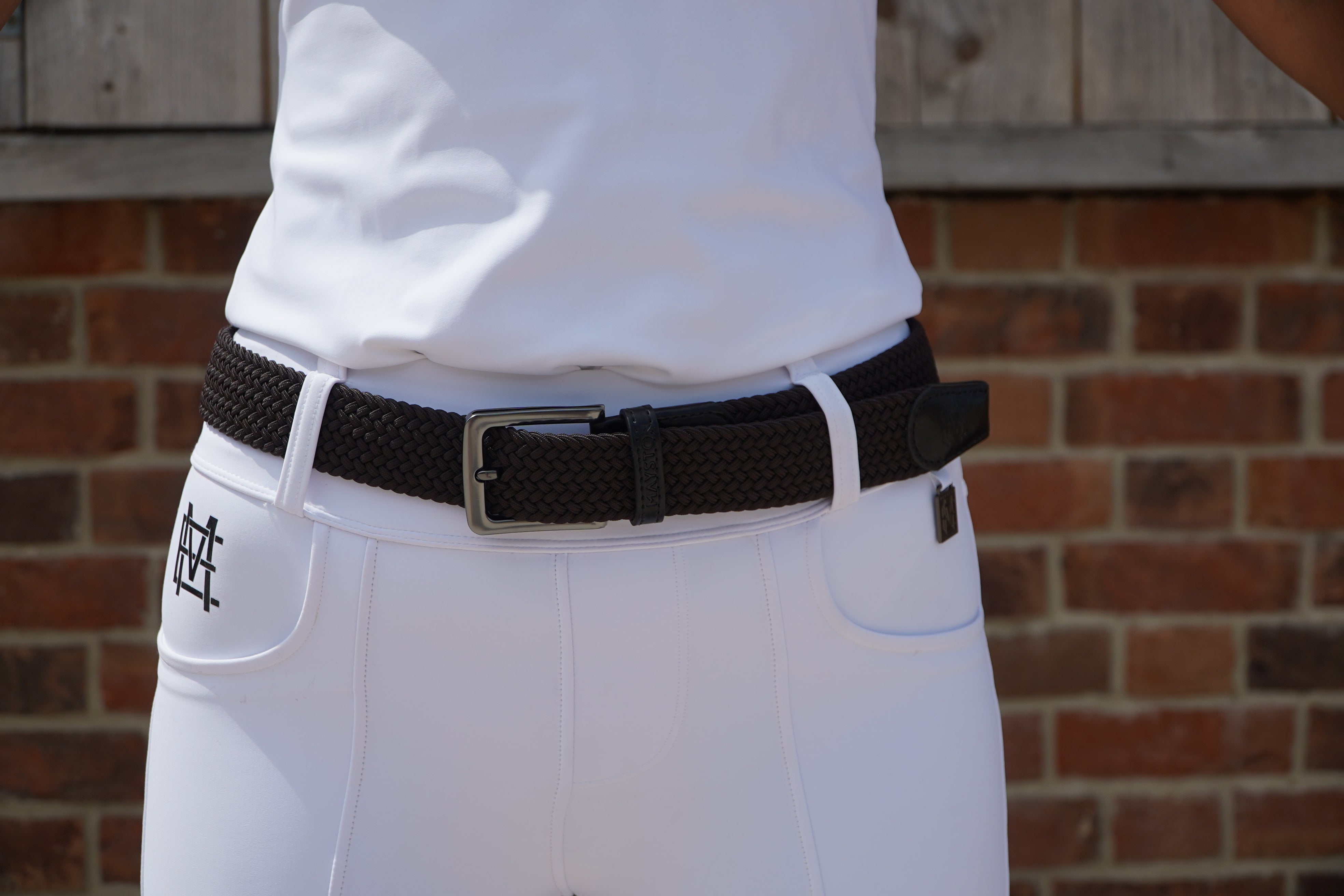 White pants with a brown belt and logo against a brick wall. Elastic stretch quality belt for casual or riding wear