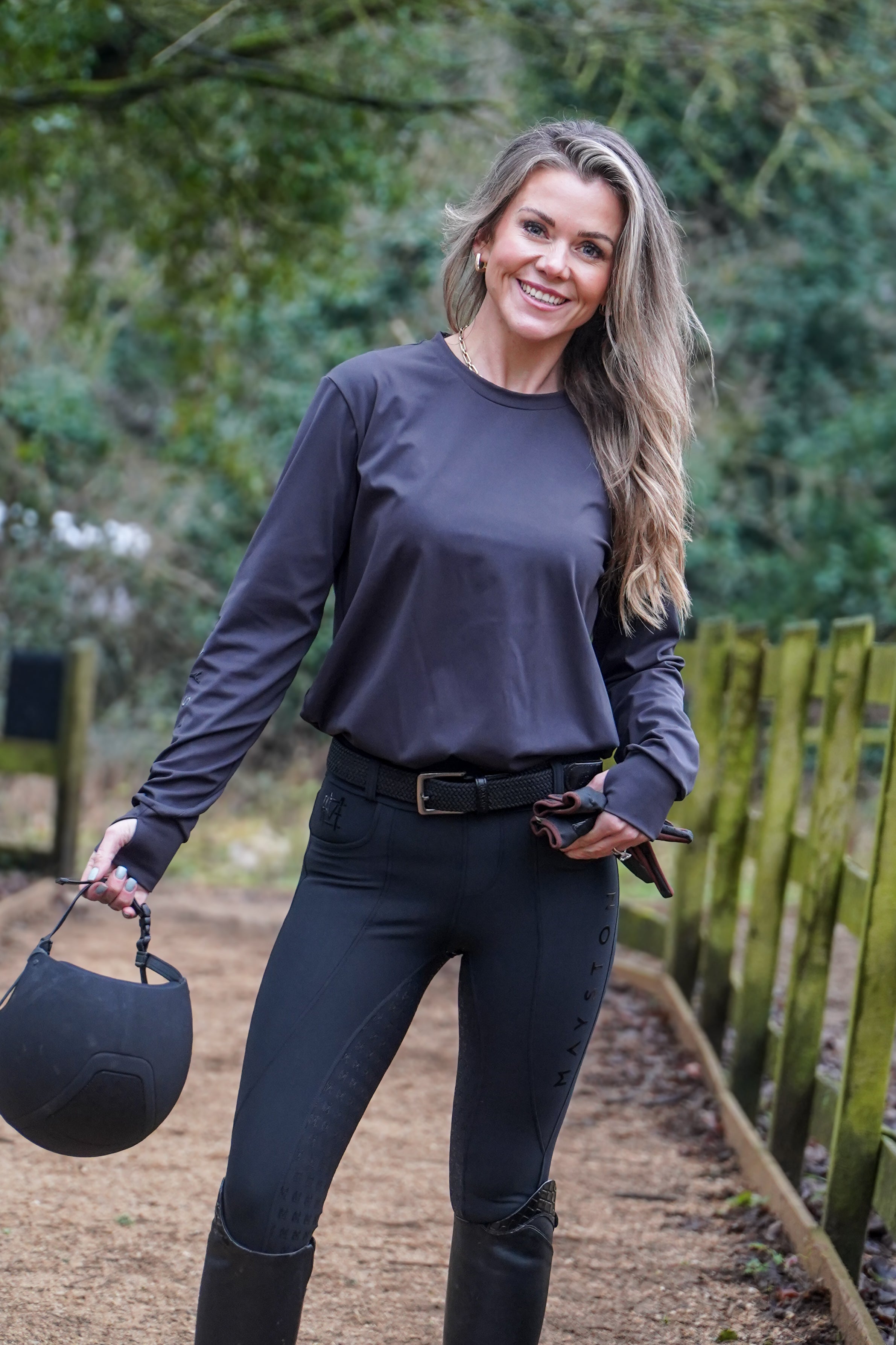 Woman in dark clothing holding a helmet outdoors with greenery in the background 
Luxury quality long sleeve t shirt and fabric is specially crafted for active duty, providing flexibility and ease of movement for any busy lifestyle. An ideal choice for a day at the yard, in the saddle, or during your grooming duties, its loose-fitting design guarantees absolute comfort. added thumbholes, Subtle branding sleek design