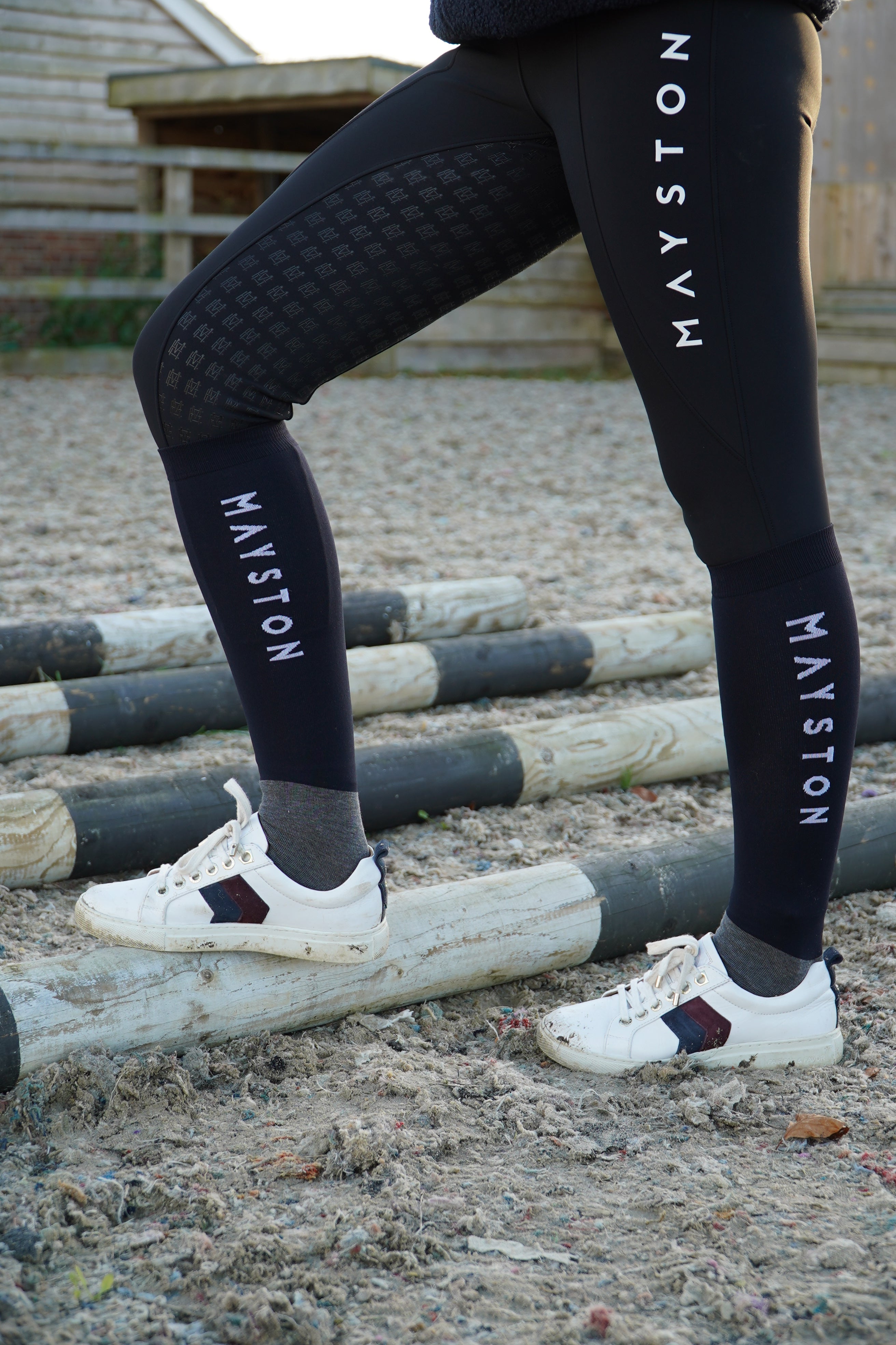 A person wearing black riding socks with the white text 'MAYSTON' on the side, standing next to a horse in an outdoor riding arena. cotton soft luxury quality socks