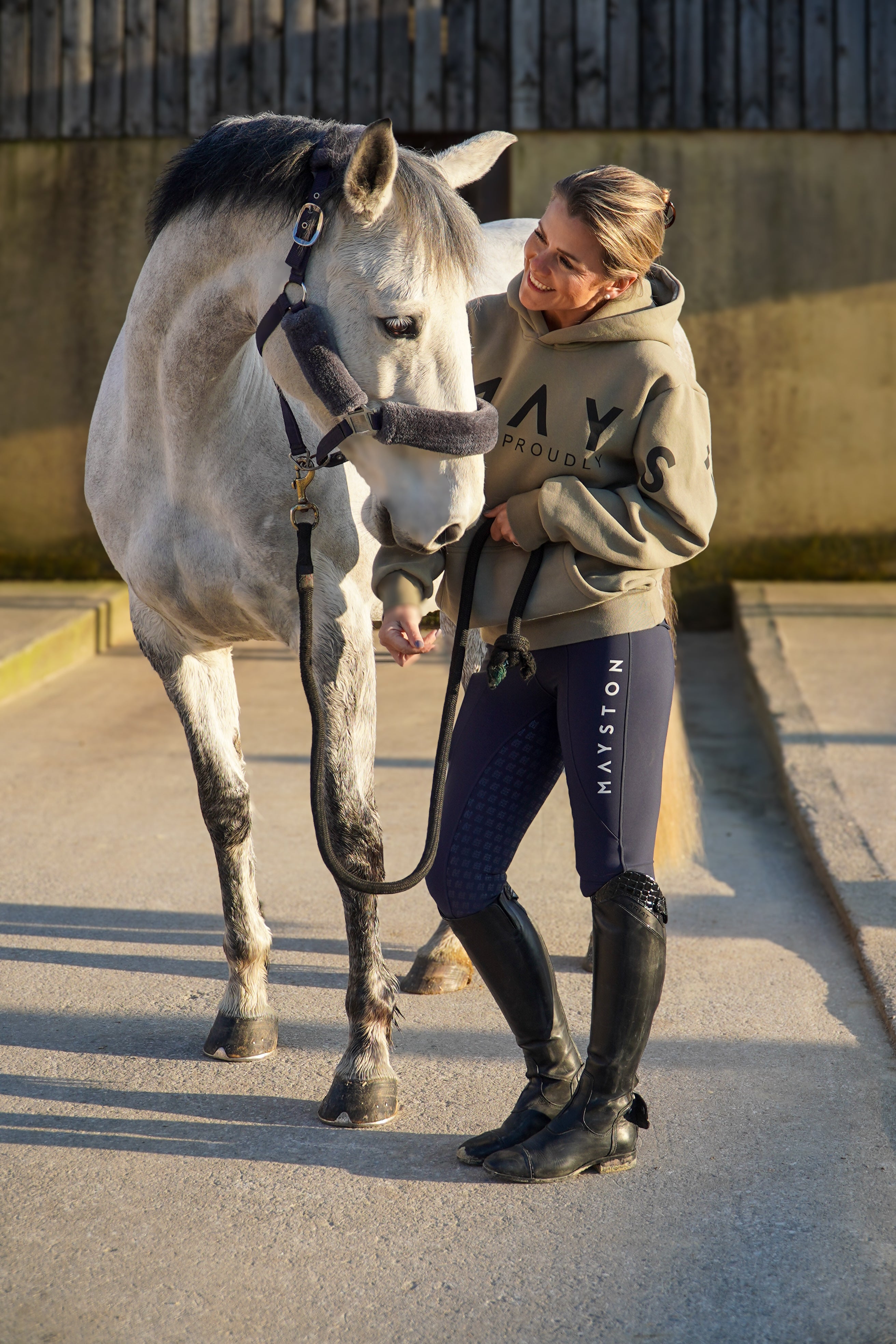 A person wearing a green hoodie with a large hood, standing next to a white horse. The person is wearing black pants and black boots, and the hoodie has the word 'Equestrian' written on it.
High quality luxurious 100% cotton. wrap around bold logo. soft, cozy and  warm. Hoodie, jumper sweatshirt. everyday wear. casual and smart